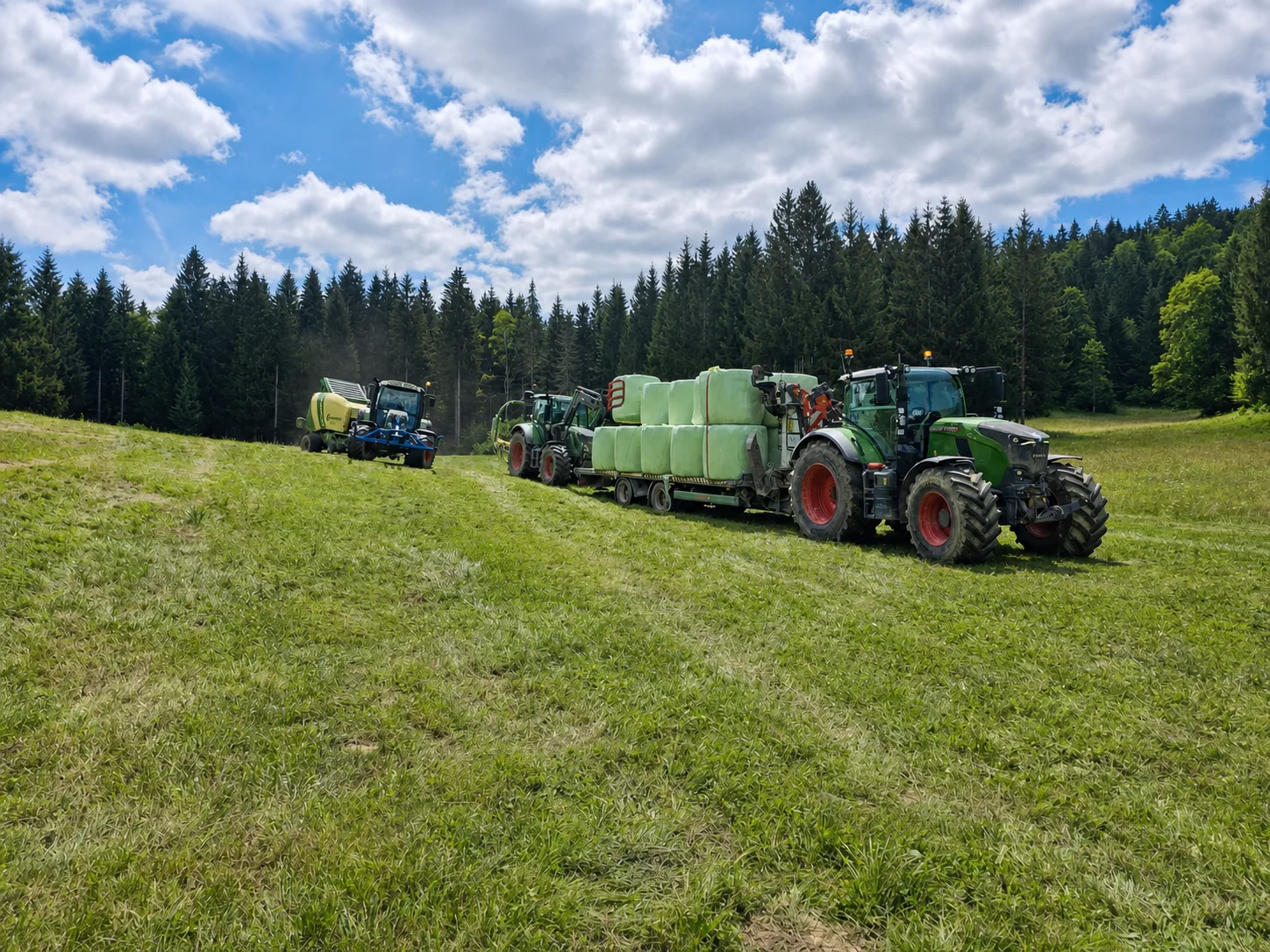 Traktorji pri spravilu ovitih bal na travniku